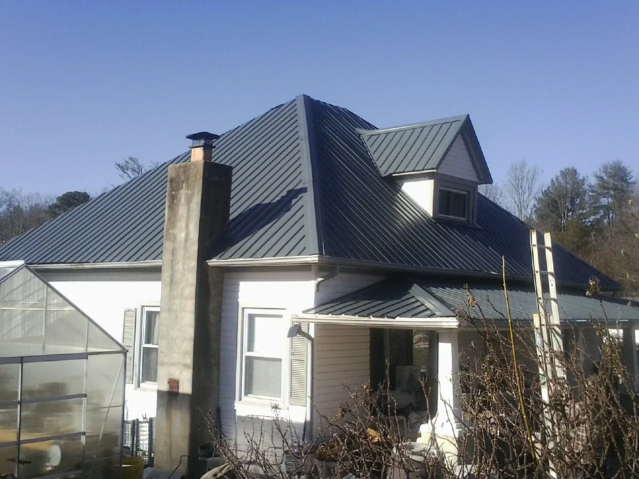 Dark blue standing seam metal roof on a white farmhouse with dormer — Slate & Tile Roof Repair by Roofing Brothers in Belmont
